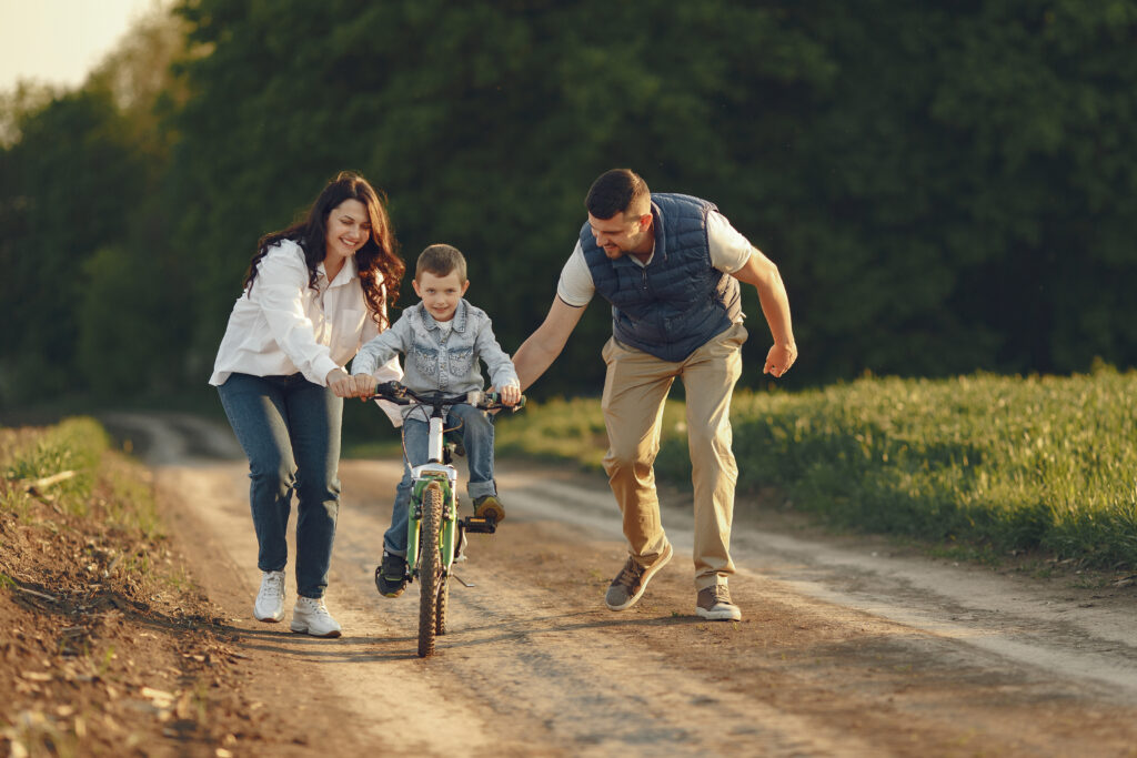 Family with cute little child. Father in a white shirt. Sunset background. Little boy ride on a bicysle.